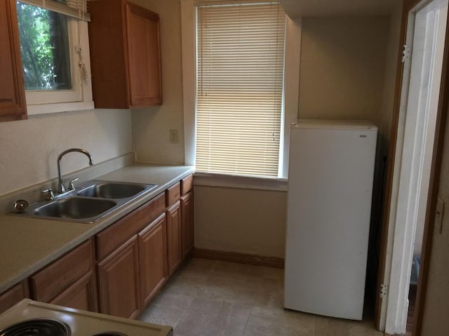 kitchen featuring a sink, light countertops, range, freestanding refrigerator, and brown cabinetry