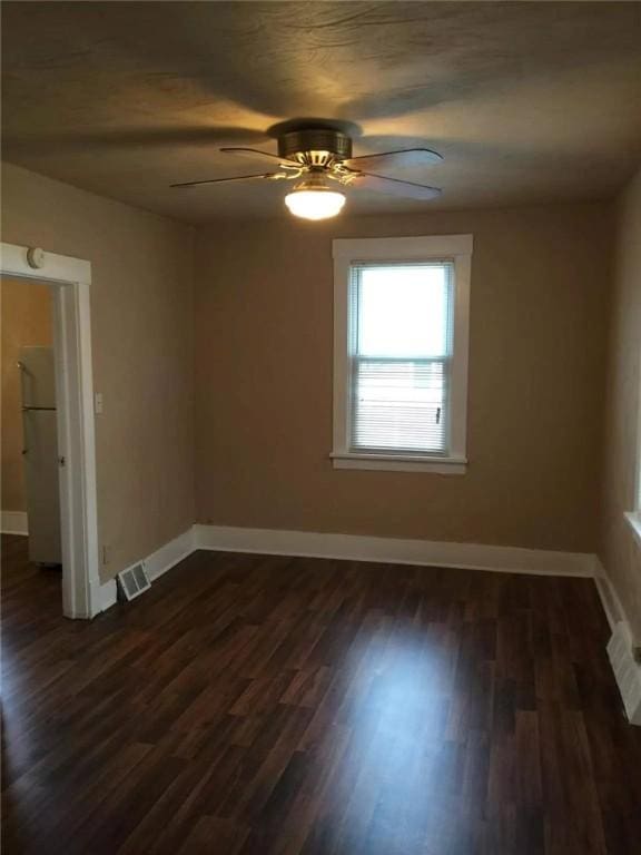 spare room featuring a ceiling fan, visible vents, dark wood finished floors, and baseboards