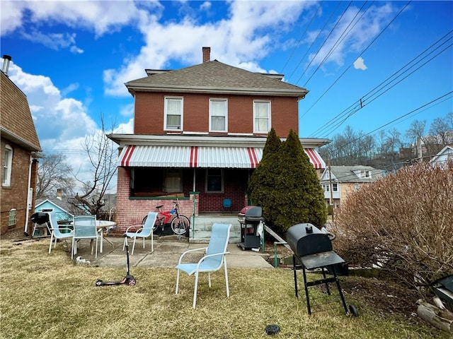 back of house with a patio area, a yard, a chimney, and brick siding