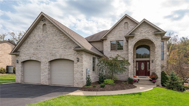 french country home with aphalt driveway, an attached garage, a front lawn, central AC, and brick siding