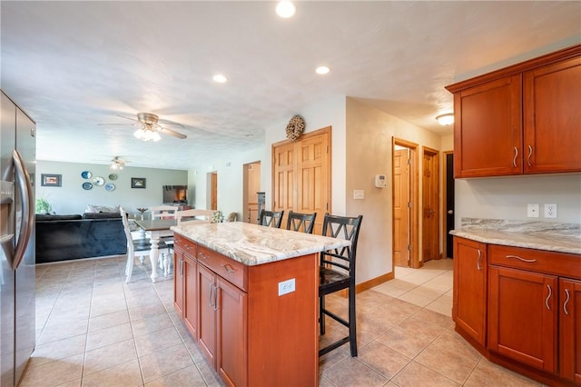 kitchen featuring stainless steel fridge, a breakfast bar area, open floor plan, light stone countertops, and light tile patterned flooring