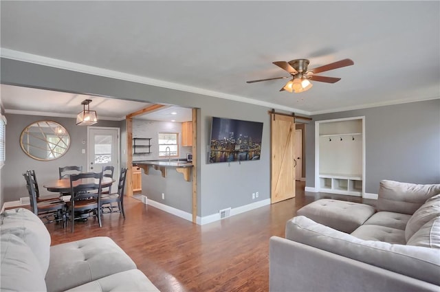 living room featuring dark wood-type flooring, visible vents, crown molding, and a barn door