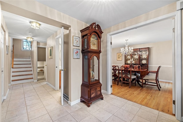 hallway featuring light tile patterned floors, a chandelier, stairs, and baseboards