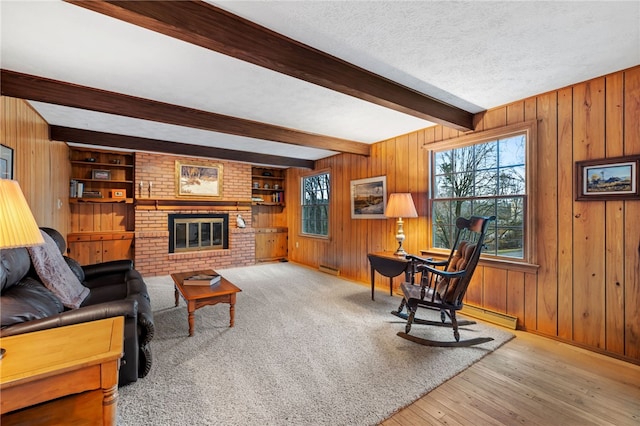 living room with a textured ceiling, light wood-style flooring, wooden walls, a brick fireplace, and beam ceiling