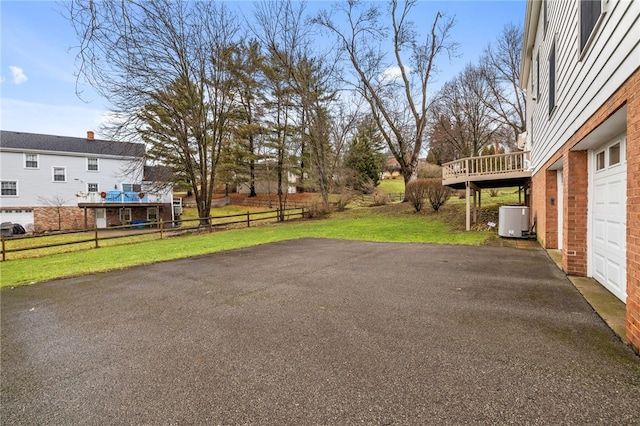 view of yard with driveway, a garage, fence, and a wooden deck