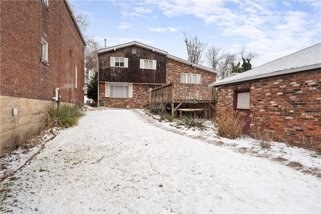 snow covered rear of property with a wooden deck and brick siding