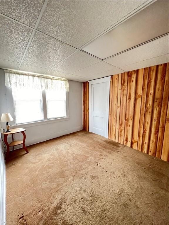 interior space featuring carpet floors, wooden walls, and a paneled ceiling