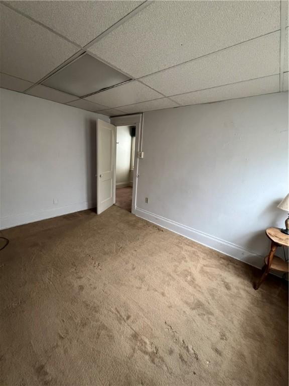 carpeted spare room with a drop ceiling and baseboards