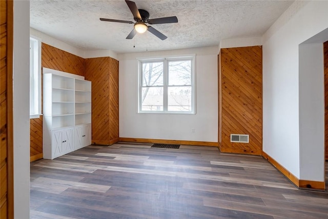 interior space featuring wood walls, visible vents, dark wood-style flooring, and a textured ceiling