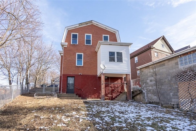 snow covered rear of property featuring fence, a gambrel roof, and brick siding