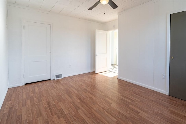 unfurnished room featuring baseboards, wood finished floors, visible vents, and a ceiling fan