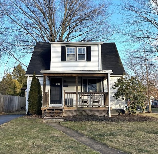 view of front of house featuring covered porch, fence, and a front lawn