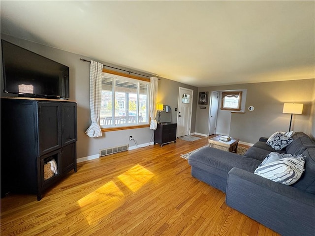 living area featuring a healthy amount of sunlight, visible vents, light wood-style flooring, and baseboards