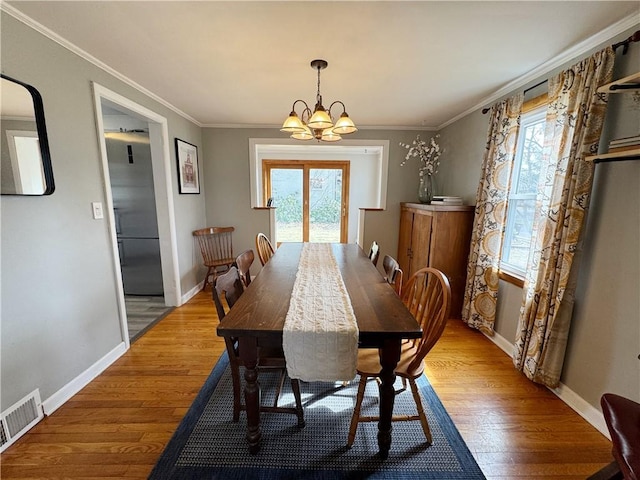 dining area featuring crown molding, visible vents, a chandelier, and wood finished floors