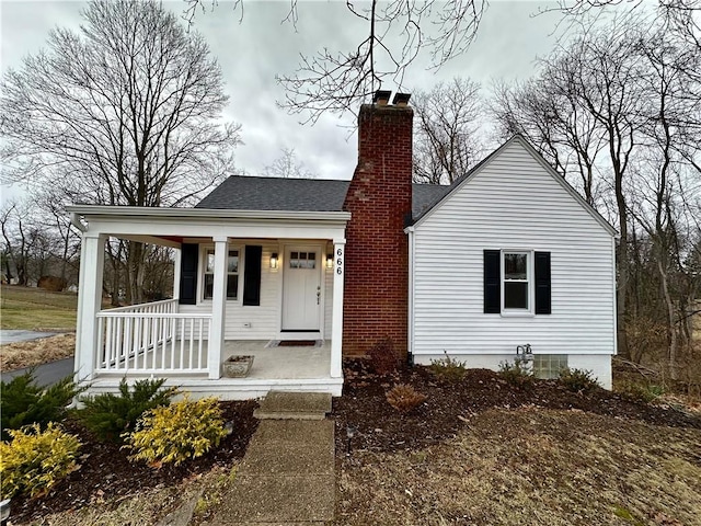 bungalow with a chimney, a porch, and roof with shingles