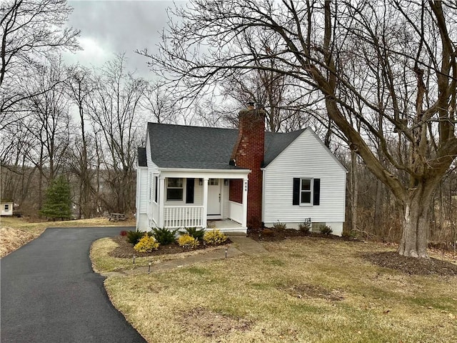 view of front of home with a porch, a front yard, driveway, and a chimney