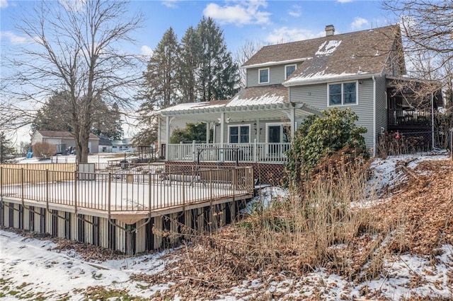 snow covered house with roof with shingles, a chimney, a wooden deck, and a pergola