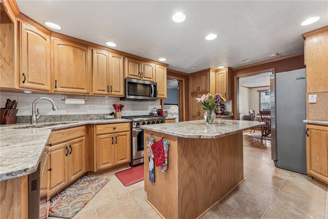 kitchen with stainless steel appliances, light stone counters, a sink, and a center island