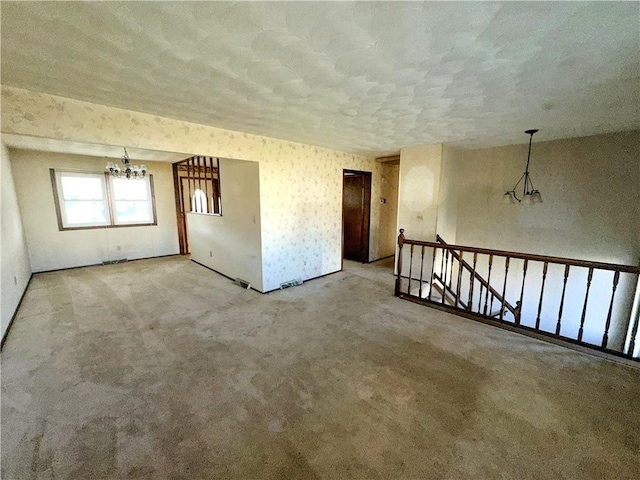 carpeted spare room featuring wallpapered walls, a textured ceiling, and an inviting chandelier