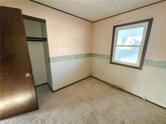 unfurnished bedroom with ornamental molding, a closet, carpet, and visible vents