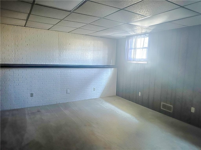 empty room with a paneled ceiling, visible vents, and brick wall