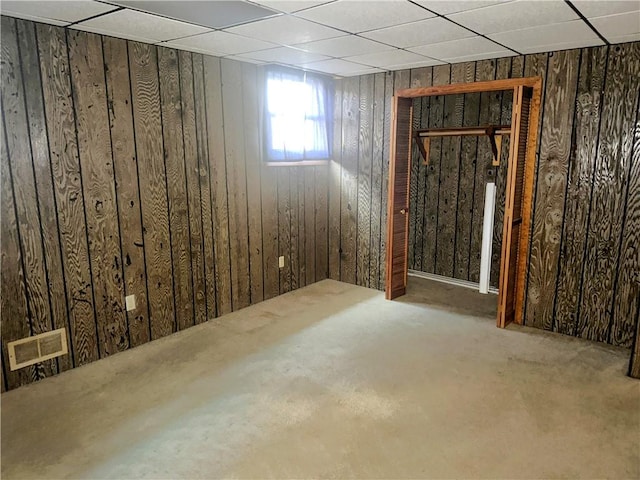 interior space featuring a paneled ceiling, wood walls, and visible vents