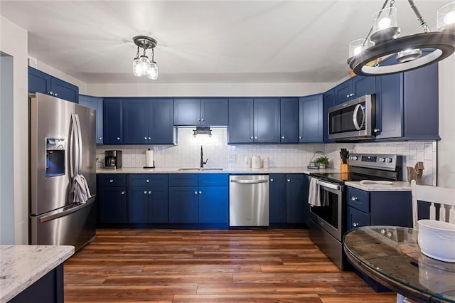 kitchen featuring pendant lighting, dark wood-style flooring, appliances with stainless steel finishes, a sink, and blue cabinets