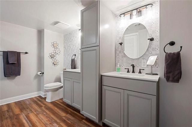 full bath with baseboards, toilet, wood finished floors, a sink, and two vanities