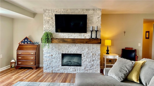 living room with light wood-style floors, baseboards, and a stone fireplace