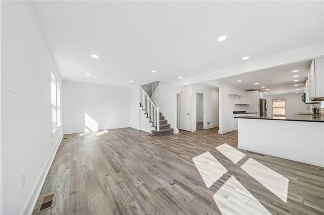 unfurnished living room featuring light wood finished floors, stairs, visible vents, and a sink