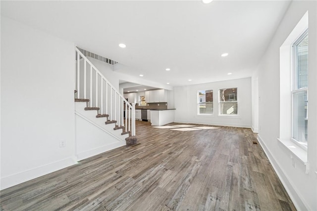 unfurnished living room with recessed lighting, wood finished floors, baseboards, and stairs