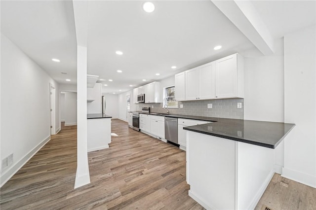 kitchen with a peninsula, dark countertops, appliances with stainless steel finishes, and white cabinets