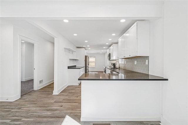 kitchen with open shelves, dark countertops, freestanding refrigerator, white cabinetry, and a peninsula