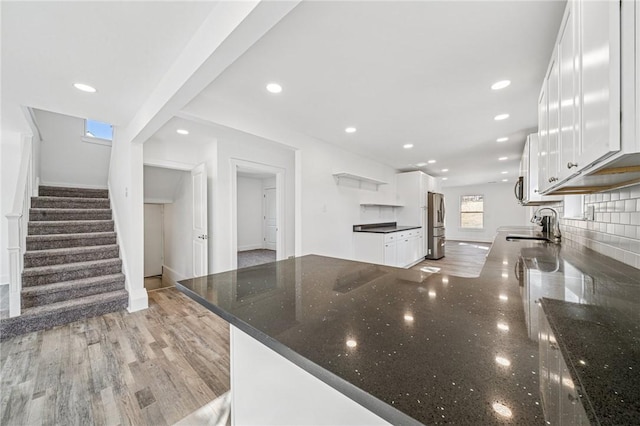 kitchen with a peninsula, a sink, white cabinets, decorative backsplash, and open shelves