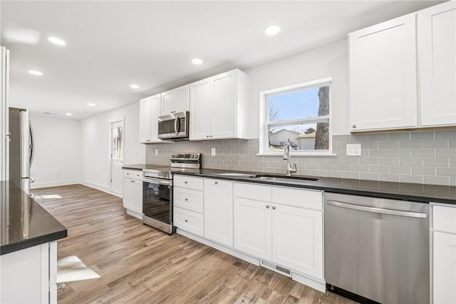 kitchen with light wood finished floors, appliances with stainless steel finishes, a sink, and white cabinetry