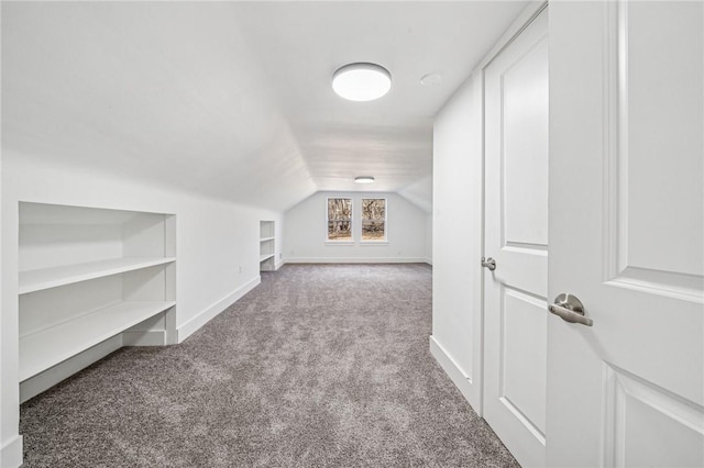 additional living space featuring built in shelves, lofted ceiling, light colored carpet, and baseboards