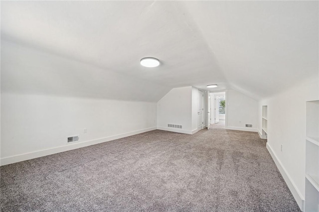 additional living space featuring built in features, visible vents, vaulted ceiling, and carpet flooring