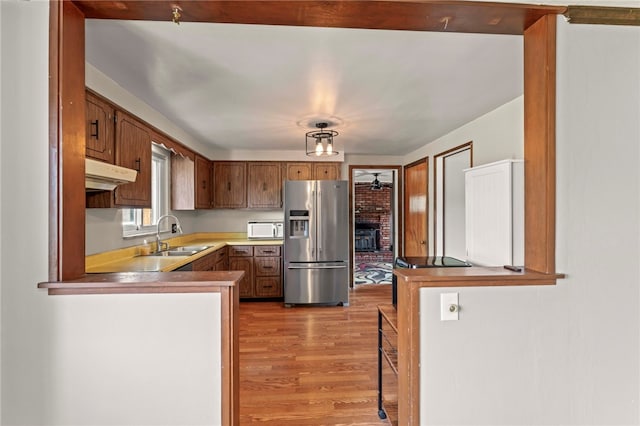 kitchen featuring brown cabinetry, white microwave, under cabinet range hood, stainless steel refrigerator with ice dispenser, and a sink