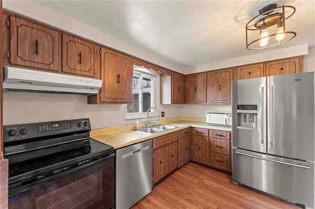 kitchen featuring under cabinet range hood, a sink, light countertops, appliances with stainless steel finishes, and brown cabinets