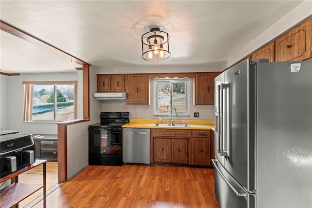 kitchen with stainless steel appliances, light countertops, brown cabinetry, a sink, and under cabinet range hood