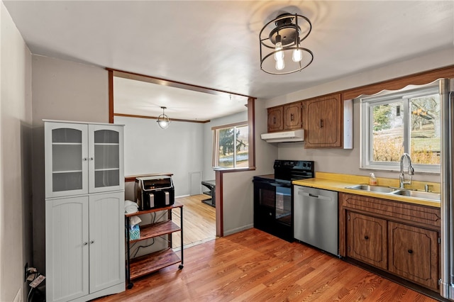 kitchen featuring black / electric stove, under cabinet range hood, a sink, dishwasher, and brown cabinetry