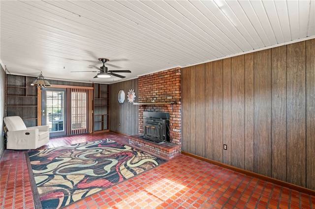 unfurnished living room featuring a wood stove, wood walls, baseboards, and a ceiling fan