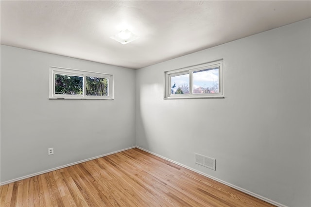 empty room featuring a healthy amount of sunlight, visible vents, light wood-style flooring, and baseboards