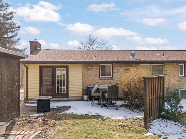 snow covered back of property with a shingled roof, central AC, a patio area, and a chimney