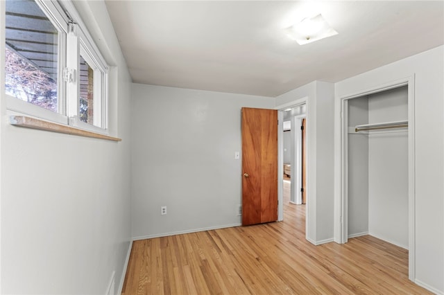 unfurnished bedroom featuring light wood finished floors, baseboards, and a closet