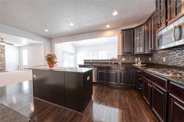 kitchen with stainless steel appliances, a sink, dark brown cabinets, a center island, and glass insert cabinets