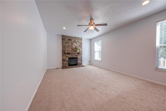 unfurnished living room with light carpet, baseboards, a ceiling fan, a textured ceiling, and a stone fireplace