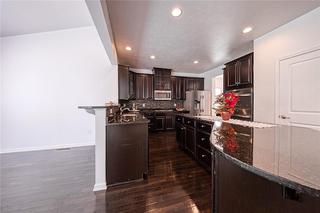 kitchen featuring dark brown cabinetry, a breakfast bar, appliances with stainless steel finishes, decorative backsplash, and glass insert cabinets