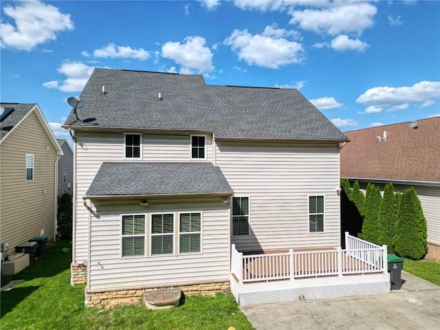 back of house featuring roof with shingles, a wooden deck, and a lawn