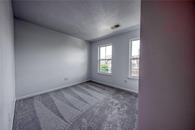 unfurnished room with a textured ceiling, carpet flooring, visible vents, and baseboards